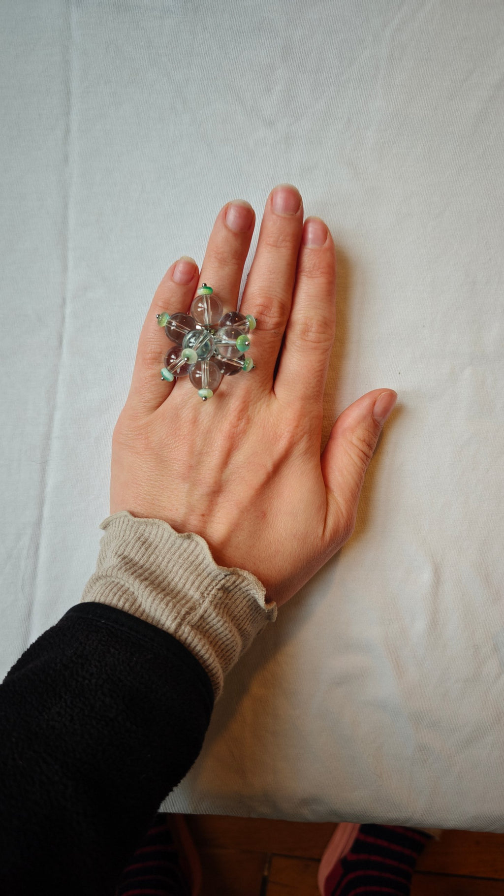 Bague ajustable en perles de verre transparentes et turquoise, portée sur la main