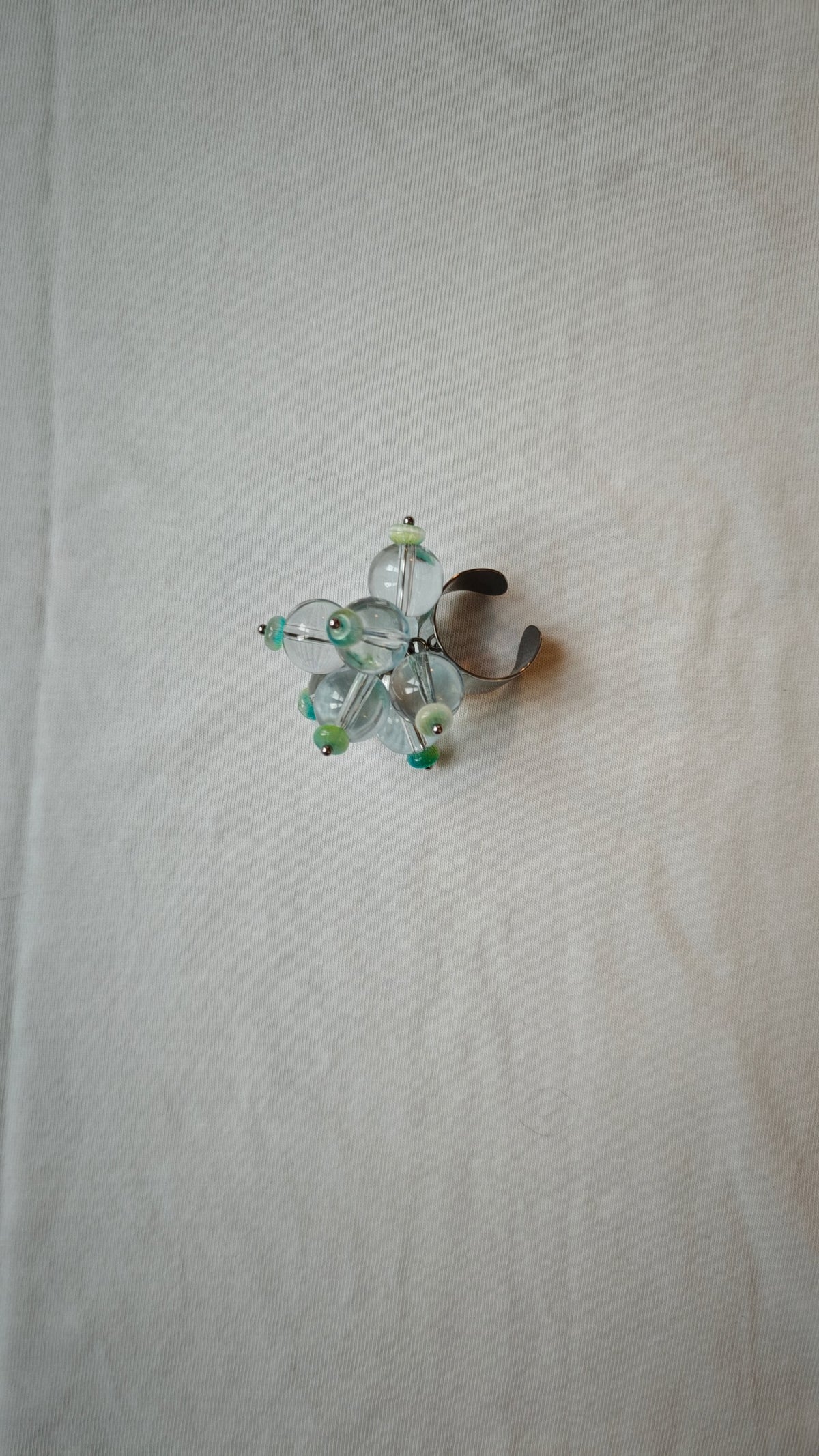 Bague ajustable en perles de verre transparentes et rondelles turquoise, posée à plat