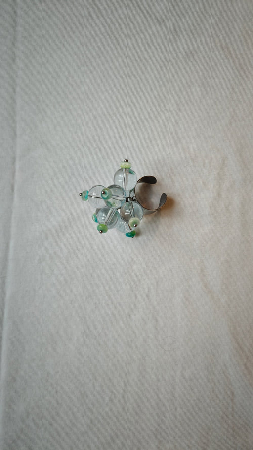 Bague ajustable en perles de verre transparentes et rondelles turquoise, posée à plat