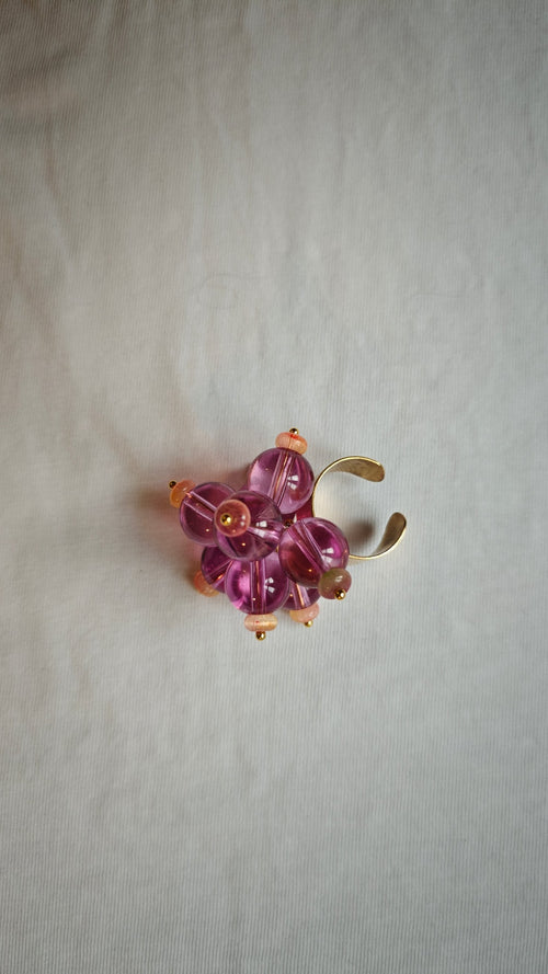 Bague ajustable ornée d'une grappe de perles de verre roses et violettes avec rondelles pêche et monture dorée, posée à plat