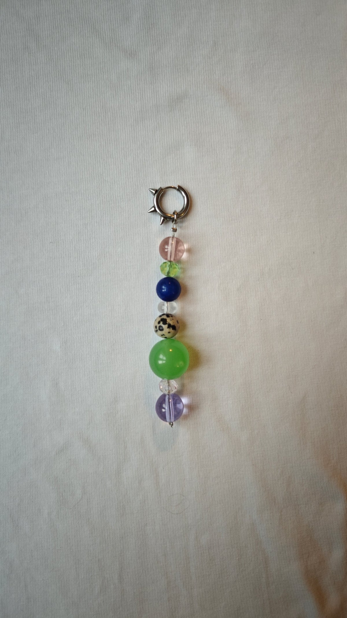 Mono boucle d'oreille composée de perles multicolores dont une perle dalmatienne et une grosse perle verte, avec anneau à pics