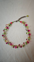Collier de gouttes de verre fuchsia, roses, vertes, ambrées et transparentes, posé à plat