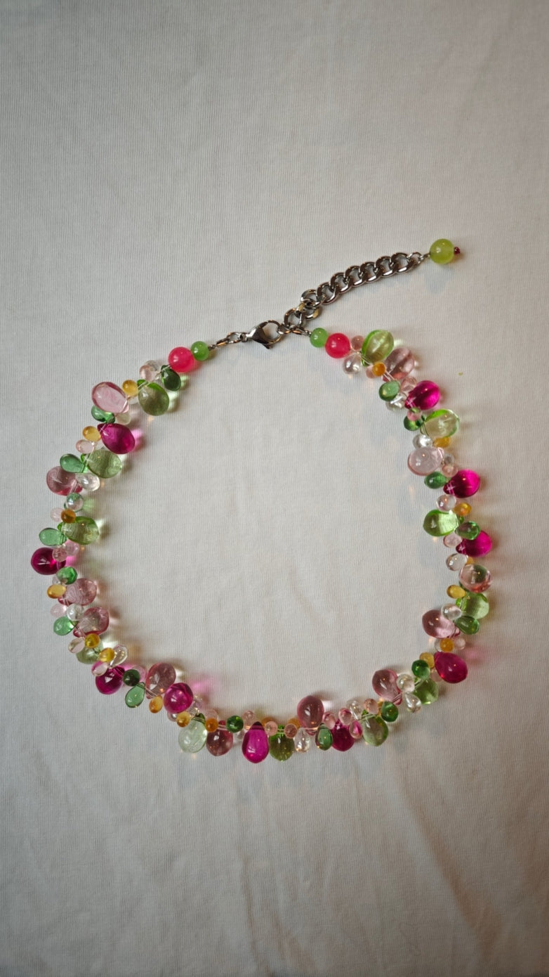 Collier de gouttes de verre fuchsia, roses, vertes, ambrées et transparentes, posé à plat