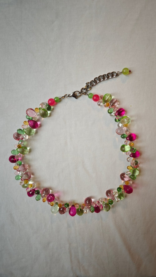 Collier de gouttes de verre fuchsia, roses, vertes, ambrées et transparentes, posé à plat