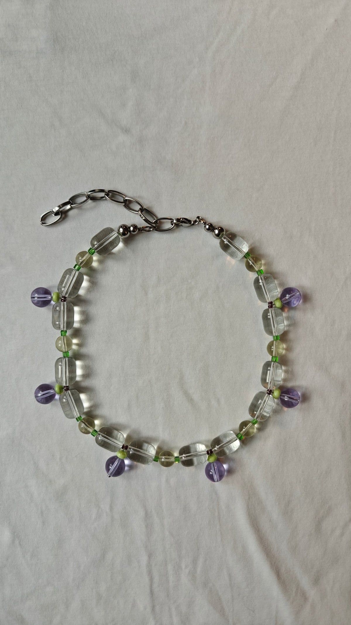 Collier de perles transparentes et vert pâle avec des pampilles rondes lilas, posé à plat