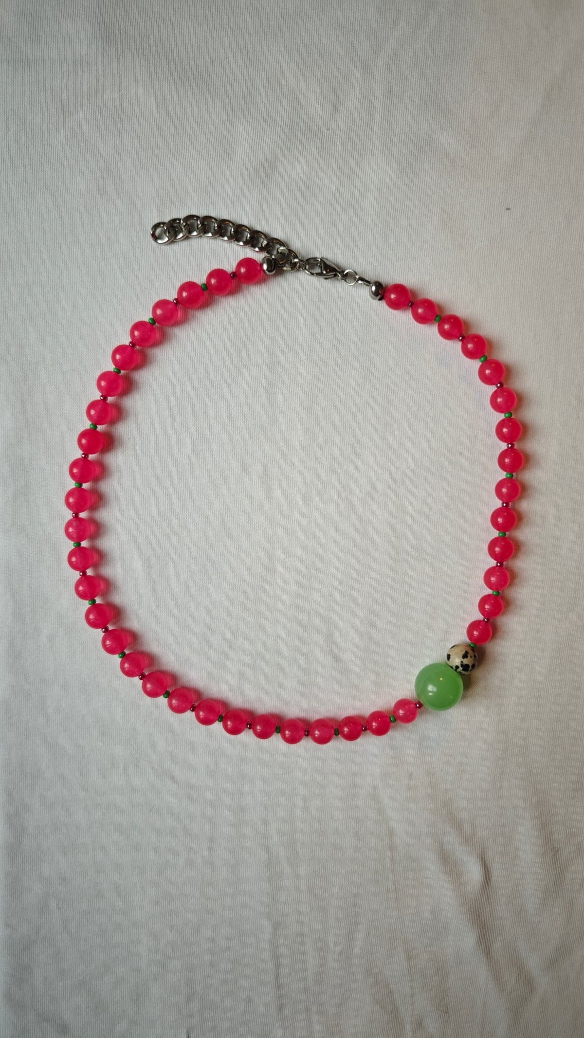 Collier de perles rondes fuchsia avec une grosse perle verte et une perle dalmatienne, posé à plat